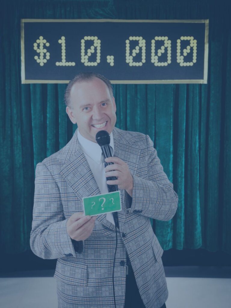 Gameshow Host smiling with microphone on his set.