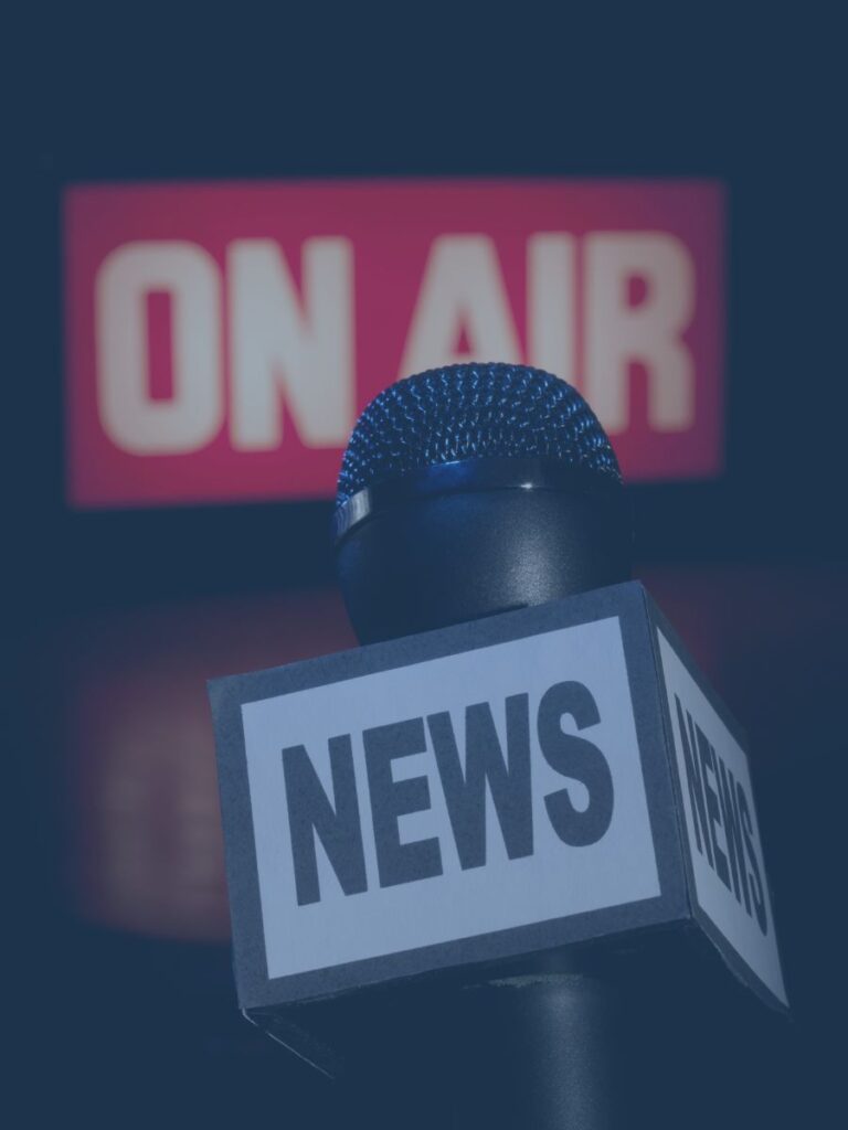 Microphone with news written on it and an on air sign on wall in back.