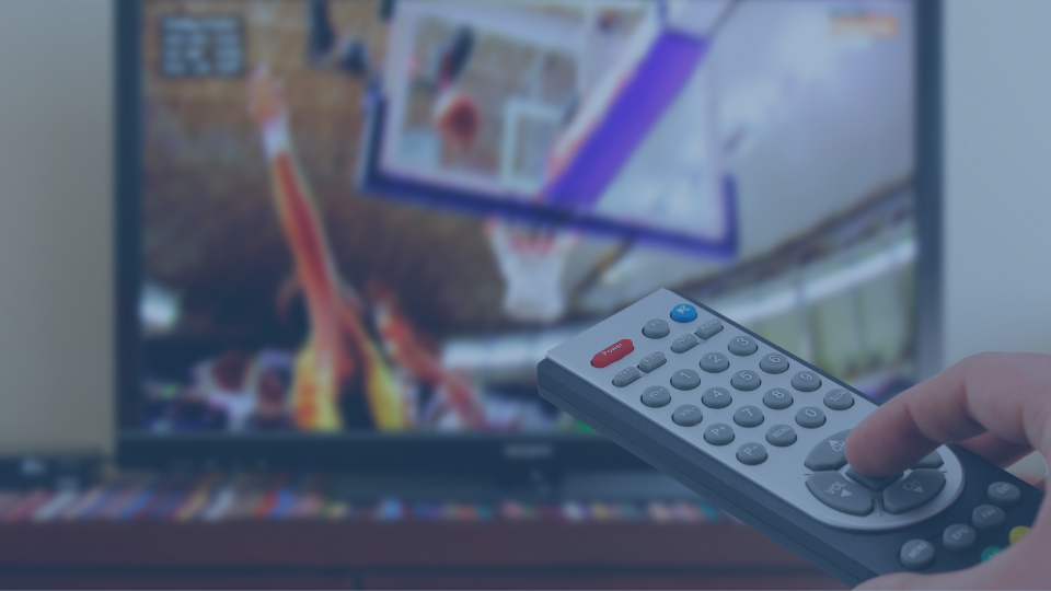 Hand holding remove pointing toward tv with basketball game on the screen.
